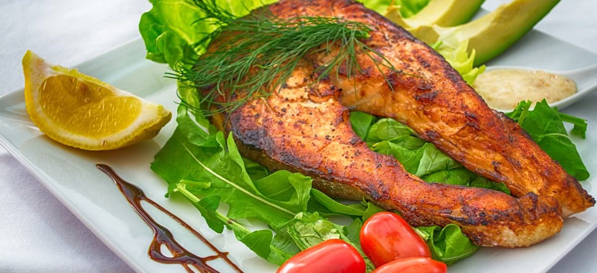 Delicious grilled salmon served with fresh vegetables and herbs on a white plate.