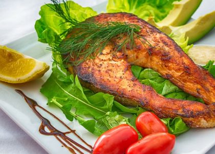 Delicious grilled salmon served with fresh vegetables and herbs on a white plate.